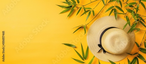 A straw hat decorated with fresh green bamboo leaves, small branches, and slender tapered leaves on a yellow backdrop with copy space image. photo