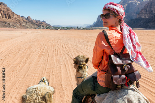 Female tourist looking over shoulder while riding on camel in desert photo