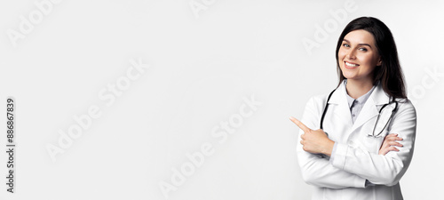 Obraz na plátne A smiling female doctor in a white coat points to the right with her right hand