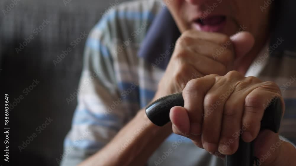 Caucasian elderly man 70 years old coughs into his fist while sitting with a walking cane while inside Caucasian elderly man 70 years old coughs into his fist while sitting with a walking cane while inside