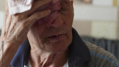 Caucasian elderly man 70 -79 years old wipes sweat from his forehead with a handkerchief while inside photo