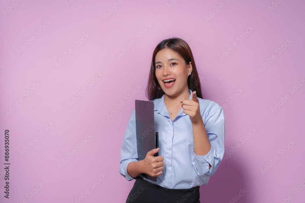Asian businesswoman holding a clipboard is pointing her finger at the viewer with a confident expression, suggesting she has a solution or an idea