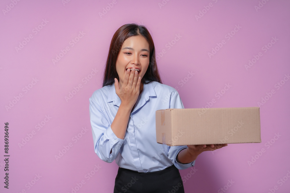 Young asian woman looks surprised and happy while holding a package against a pink background, perfect for concepts like delivery and online shopping Young asian woman looks surprised and happy while holding a package against a pink background, perfect for concepts like delivery and online shopping