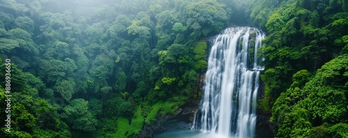 Majestic waterfall cascading through lush green forest with misty atmosphere, creating a tranquil and serene natural scene.