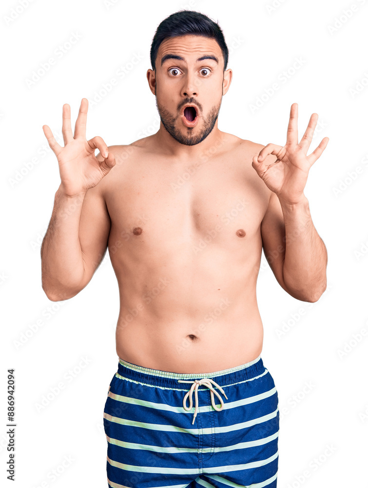 Young handsome man wearing swimwear looking surprised and shocked doing ok approval symbol with fingers. crazy expression Young handsome man wearing swimwear looking surprised and shocked doing ok approval symbol with fingers. crazy expression