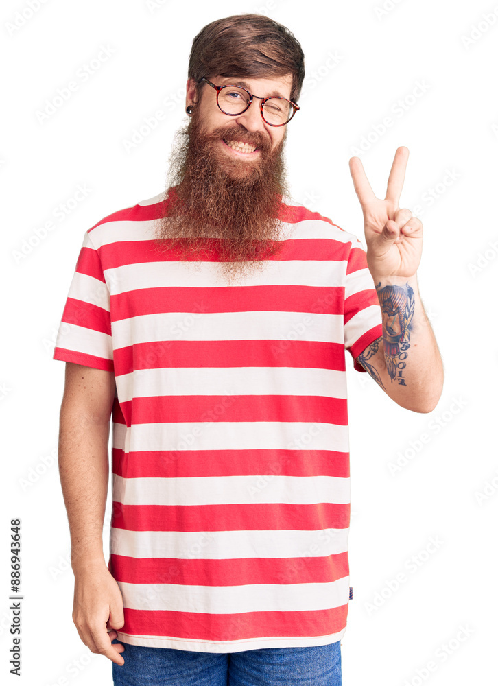 Handsome young red head man with long beard wearing casual clothes smiling with happy face winking at the camera doing victory sign. number two. Handsome young red head man with long beard wearing casual clothes smiling with happy face winking at the camera doing victory sign. number two.