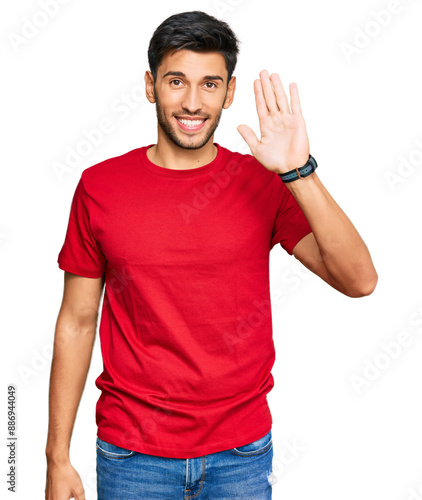 Young handsome man wearing casual red tshirt waiving saying hello happy and smiling, friendly welcome gesture photo