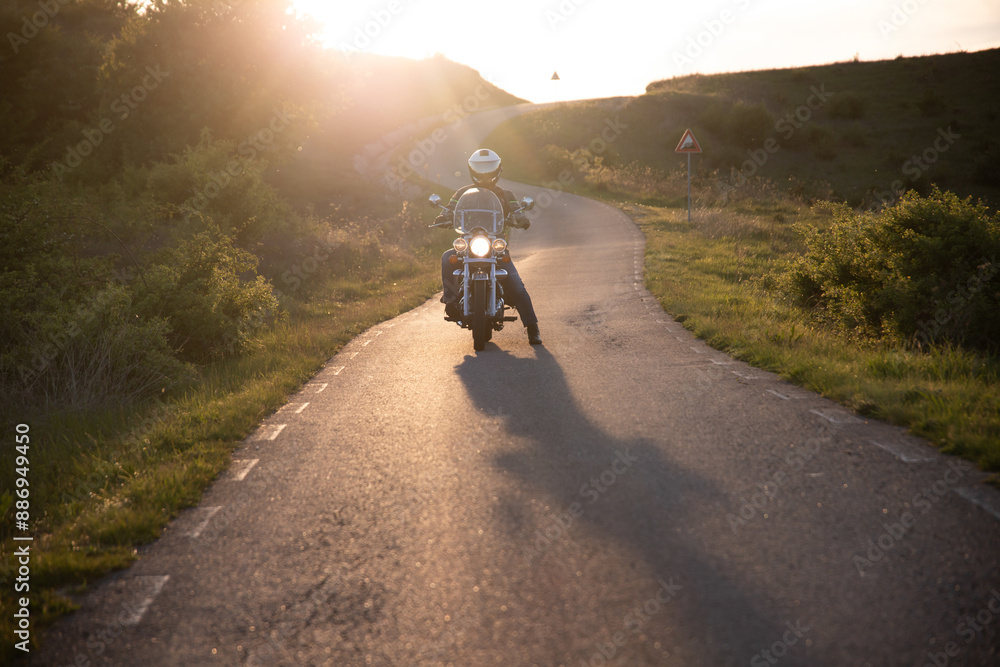 Biker driving a motorcycle rides along the asphalt road in sunset. Biker driving a motorcycle rides along the asphalt road in sunset.