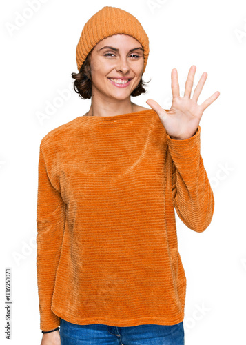 Young hispanic woman wearing casual clothes and wool cap showing and pointing up with fingers number five while smiling confident and happy.