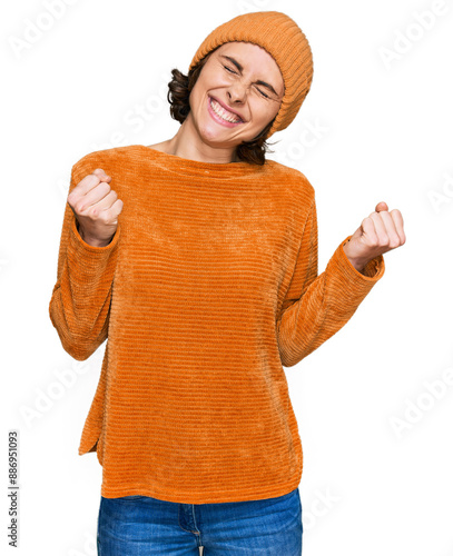 Young hispanic woman wearing casual clothes and wool cap excited for success with arms raised and eyes closed celebrating victory smiling. winner concept.