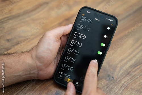 Foto Male person holds modern smartphone setting time on alarm clock app ensuring to