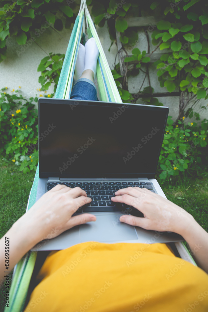Young woman sitting in a hammock in garden with laptop Young woman sitting in a hammock in garden with laptop