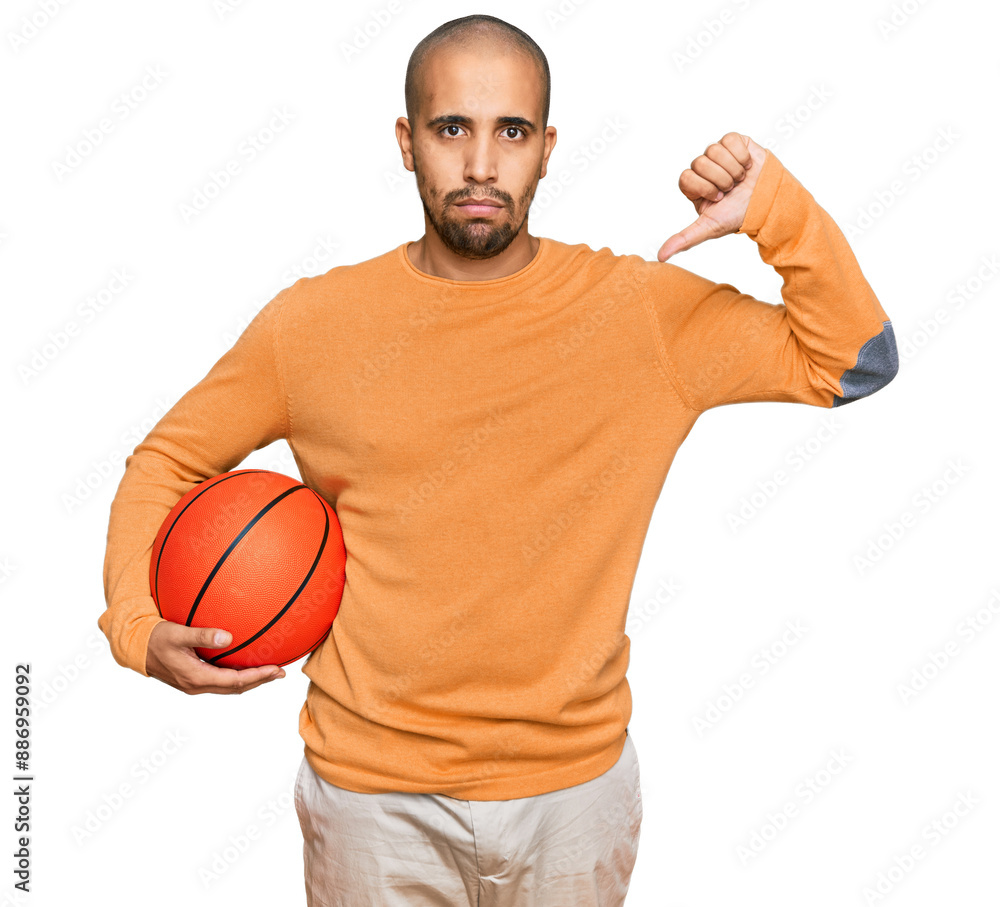 Hispanic adult man holding basketball ball with angry face, negative sign showing dislike with thumbs down, rejection concept Hispanic adult man holding basketball ball with angry face, negative sign showing dislike with thumbs down, rejection concept