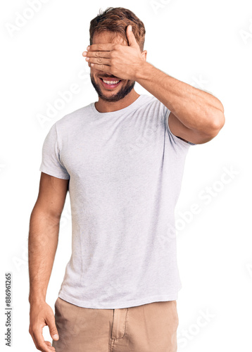 Young caucasian man wearing casual white tshirt smiling and laughing with hand on face covering eyes for surprise. blind concept.