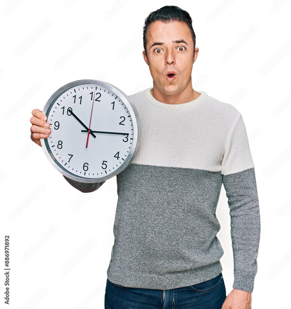 Handsome young man holding big clock scared and amazed with open mouth for surprise, disbelief face Handsome young man holding big clock scared and amazed with open mouth for surprise, disbelief face