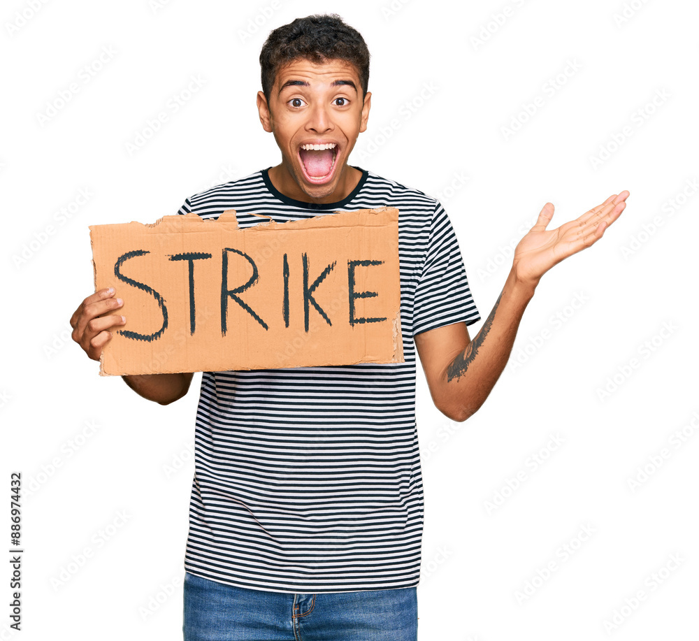 Young handsome african american man holding strike banner cardboard celebrating victory with happy smile and winner expression with raised hands Young handsome african american man holding strike banner cardboard celebrating victory with happy smile and winner expression with raised hands