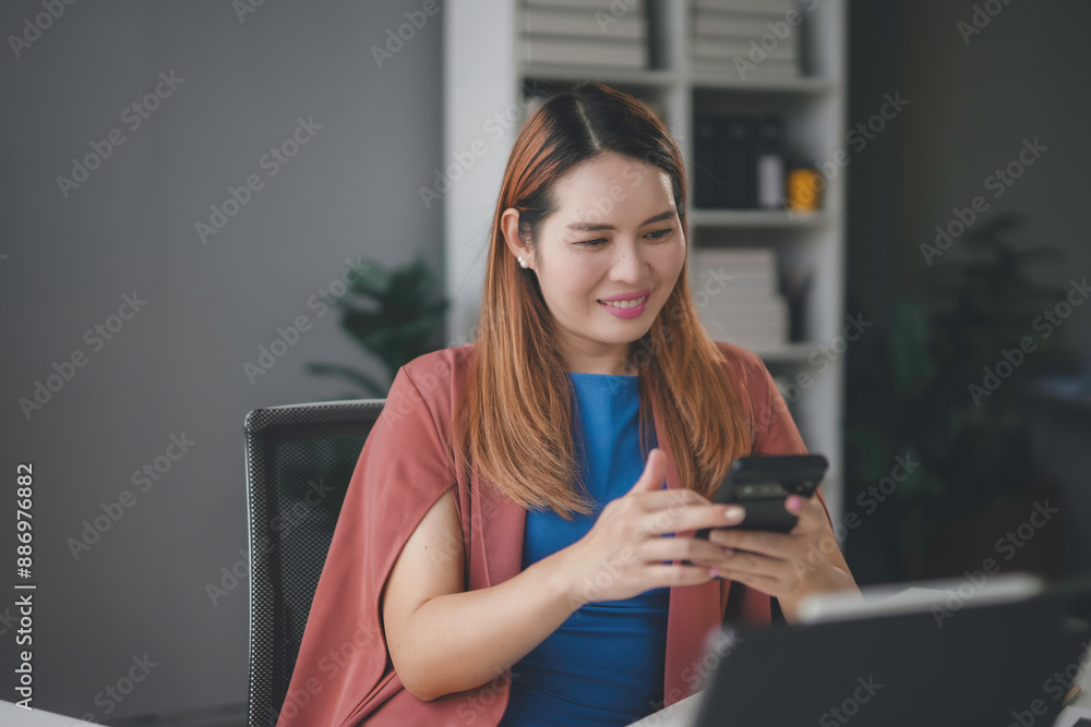 Young asian businesswoman happily uses her smartphone in a modern office, reflecting her success as an entrepreneur Young asian businesswoman happily uses her smartphone in a modern office, reflecting her success as an entrepreneur