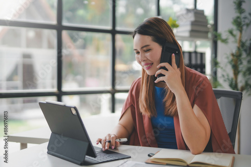 Businesswoman smiling while talking on the phone and working on a digital tablet, demonstrating efficiency and connectivity in a modern office setting