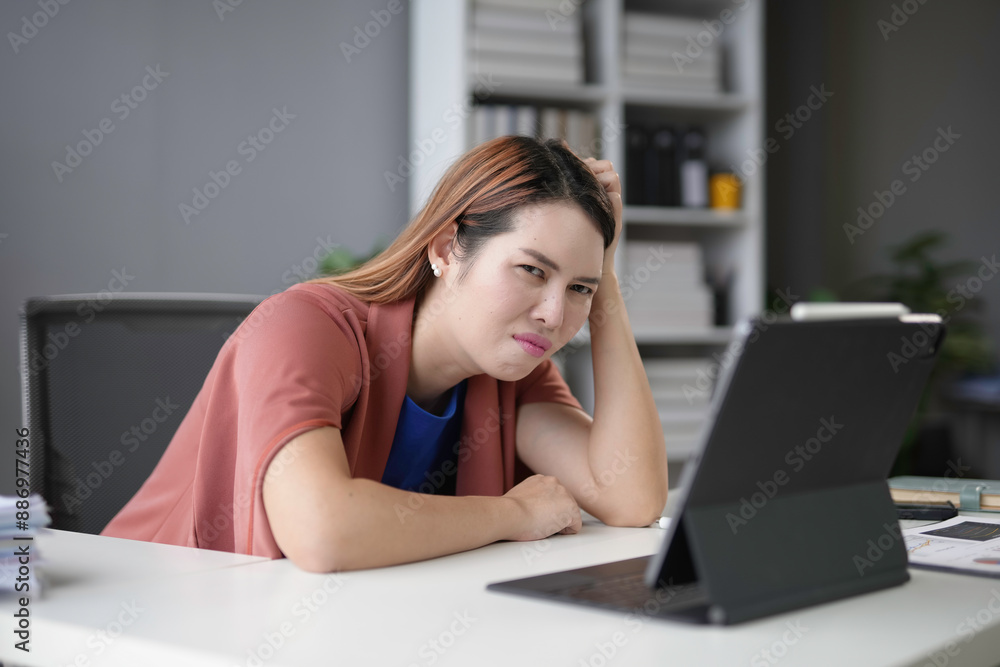Asian businesswoman is having a stressful day at work while looking at her tablet, clearly overwhelmed with her tasks Asian businesswoman is having a stressful day at work while looking at her tablet, clearly overwhelmed with her tasks