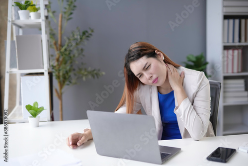 Stressed businesswoman massages neck at laptop, feeling tired and fatigued from overwork in the office. Sitting long hours can cause shoulder pain. Prioritize health to avoid issues