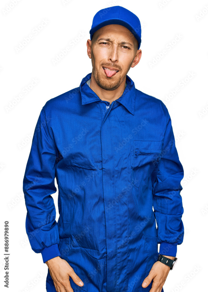 Bald man with beard wearing builder jumpsuit uniform sticking tongue out happy with funny expression. emotion concept. Bald man with beard wearing builder jumpsuit uniform sticking tongue out happy with funny expression. emotion concept.