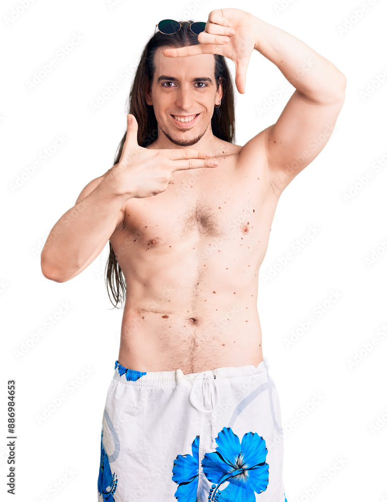 Fototapeta premium Young adult man with long hair wearing swimwear shirtless smiling making frame with hands and fingers with happy face. creativity and photography concept.