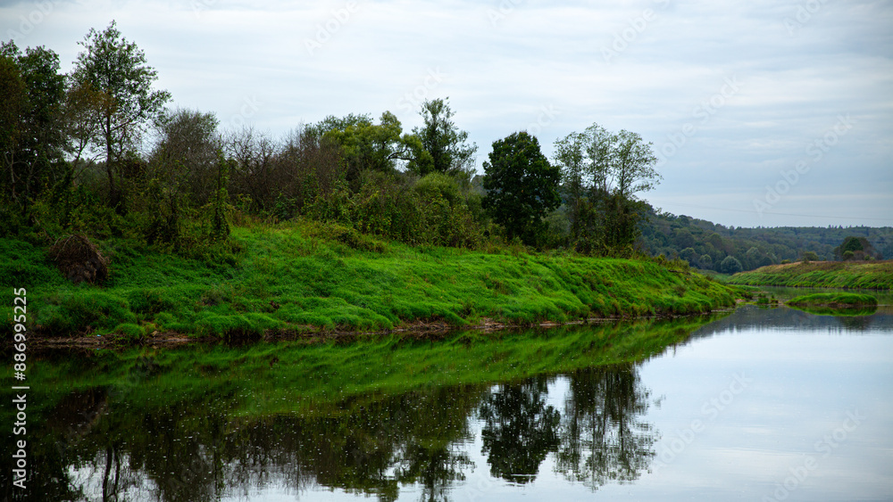 A beautiful riverbank with lush greenery and calm water reflection, creating a serene atmosphere A beautiful riverbank with lush greenery and calm water reflection, creating a serene atmosphere