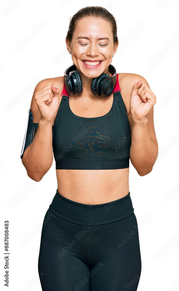 Beautiful blonde woman wearing gym clothes and using headphones excited for success with arms raised and eyes closed celebrating victory smiling. winner concept. Beautiful blonde woman wearing gym clothes and using headphones excited for success with arms raised and eyes closed celebrating victory smiling. winner concept.