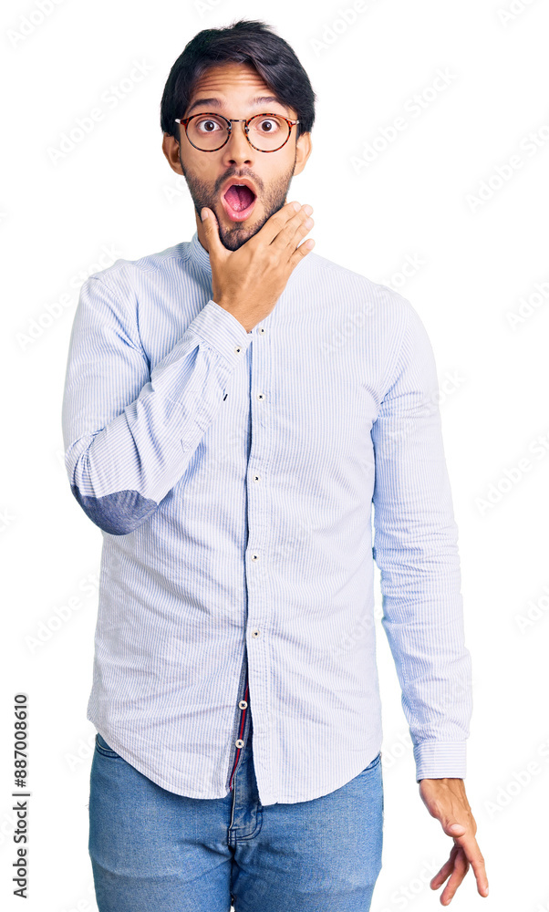 Handsome hispanic man wearing business shirt and glasses looking fascinated with disbelief, surprise and amazed expression with hands on chin Handsome hispanic man wearing business shirt and glasses looking fascinated with disbelief, surprise and amazed expression with hands on chin