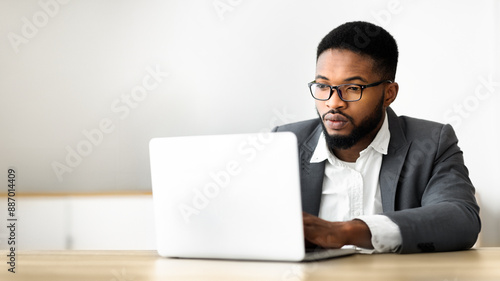 Confident african american businessman working on laptop in office, looking at screen with serious face expression, panorama with copy space