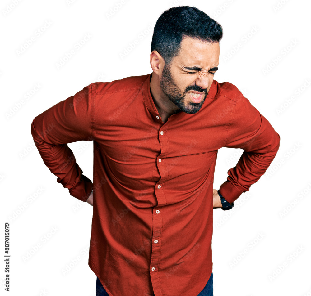 Young hispanic man with beard wearing casual shirt suffering of backache, touching back with hand, muscular pain Young hispanic man with beard wearing casual shirt suffering of backache, touching back with hand, muscular pain