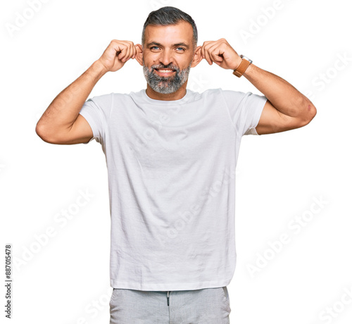 Middle age handsome man wearing casual white tshirt smiling pulling ears with fingers, funny gesture. audition problem