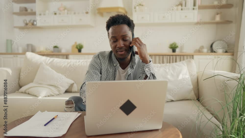 Home office of freelancer, African American man calling by phone, using laptop. Freelance and startup, employee working remotely, busy and multitasking person, distant communication with partners Home office of freelancer, African American man calling by phone, using laptop. Freelance and startup, employee working remotely, busy and multitasking person, distant communication with partners