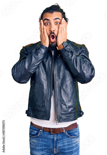 Young arab man wearing casual leather jacket afraid and shocked, surprise and amazed expression with hands on face