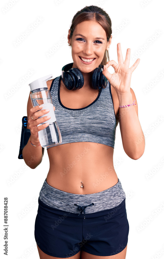 Young beautiful hispanic woman wearing sportswear holding water bottle doing ok sign with fingers, smiling friendly gesturing excellent symbol Young beautiful hispanic woman wearing sportswear holding water bottle doing ok sign with fingers, smiling friendly gesturing excellent symbol