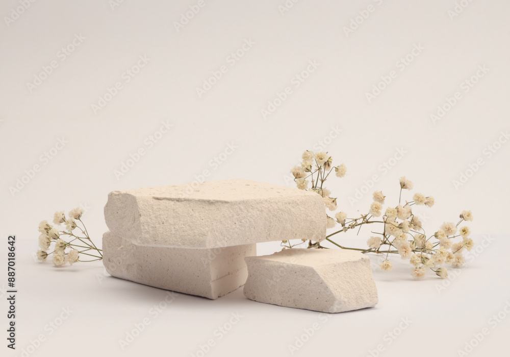 Fototapeta premium White Stones platform podium, dry flower twig on beige light background. Minimal empty display product presentation scene.
