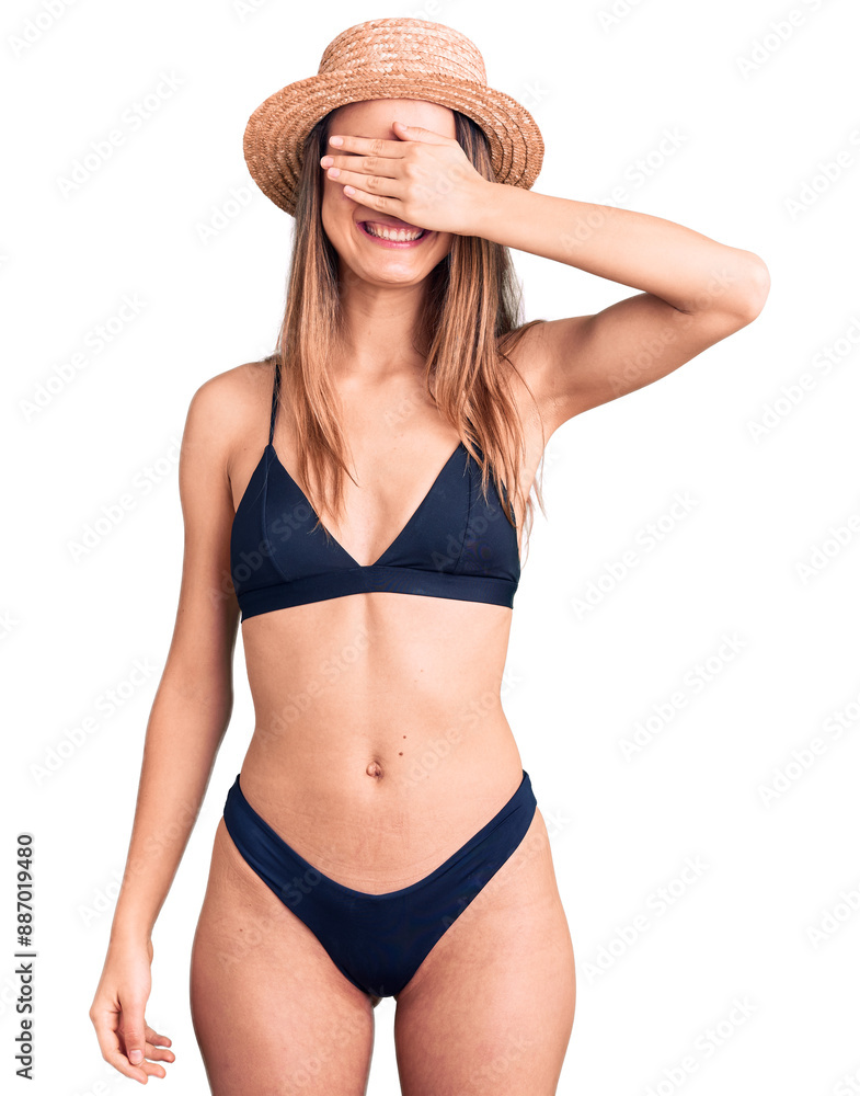 Young beautiful girl wearing bikini and hat smiling and laughing with hand on face covering eyes for surprise. blind concept. Young beautiful girl wearing bikini and hat smiling and laughing with hand on face covering eyes for surprise. blind concept.
