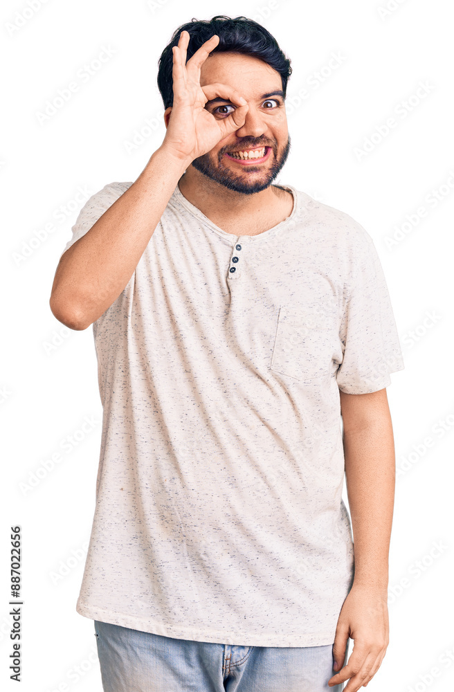 Young hispanic man wearing casual clothes doing ok gesture with hand smiling, eye looking through fingers with happy face. Young hispanic man wearing casual clothes doing ok gesture with hand smiling, eye looking through fingers with happy face.
