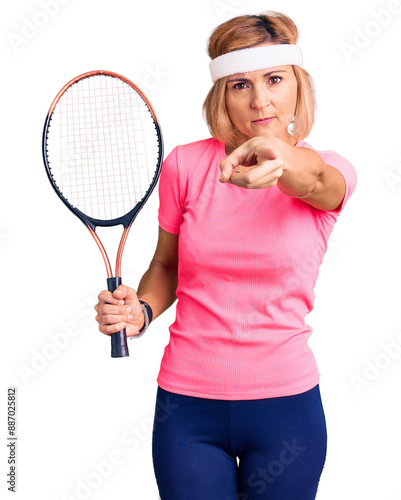 Young blonde woman playing tennis holding racket pointing with finger to the camera and to you, confident gesture looking serious