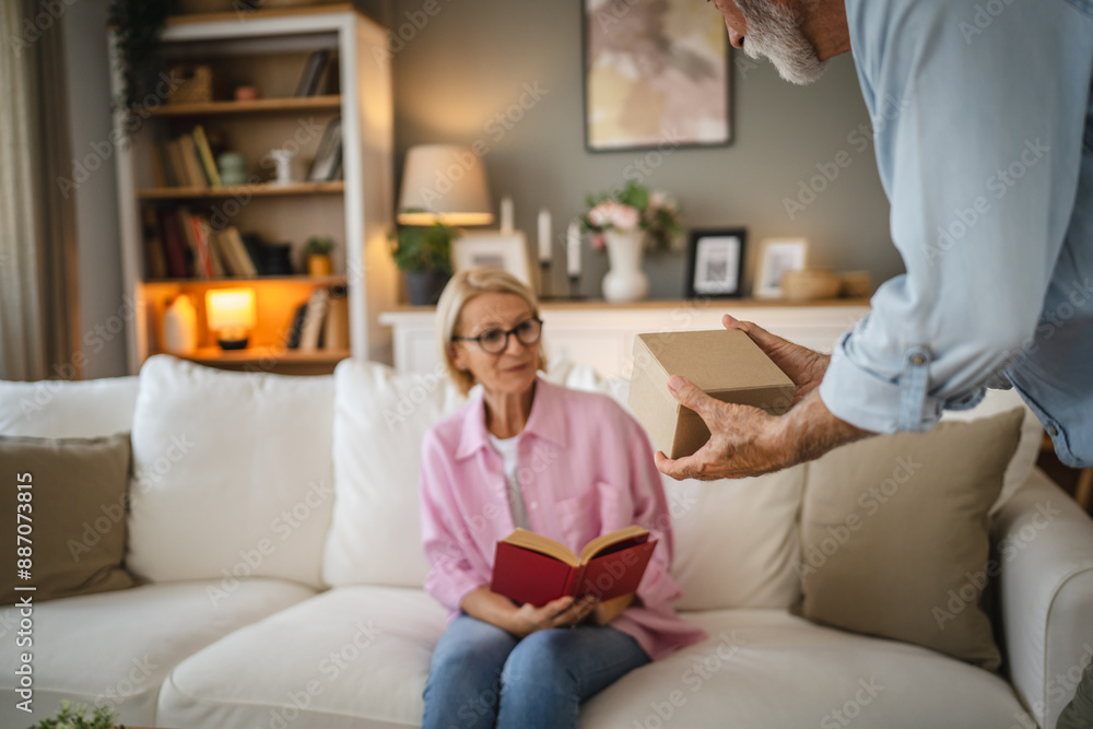 Obraz premium Senior husband surprised his mature wife whit gift while she read book
