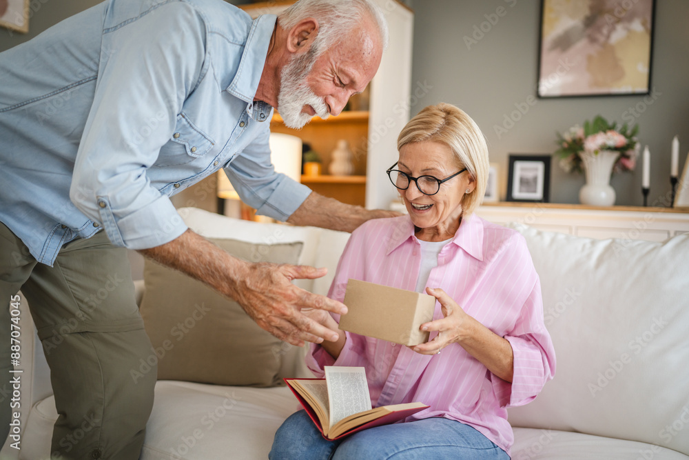 Obraz premium Senior husband surprised his mature wife whit gift while she read book