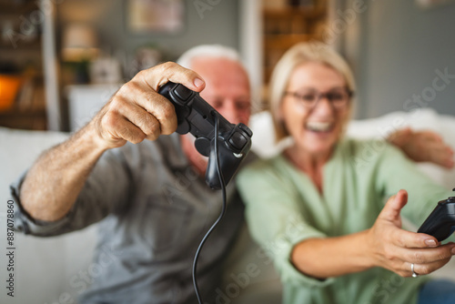 Senior couple sit on sofa and play video games on joystick at home