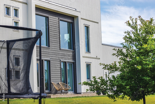 Foto Close-up view of modern European villa in village with panoramic windows, green lawn in garden, patio furniture and trampoline