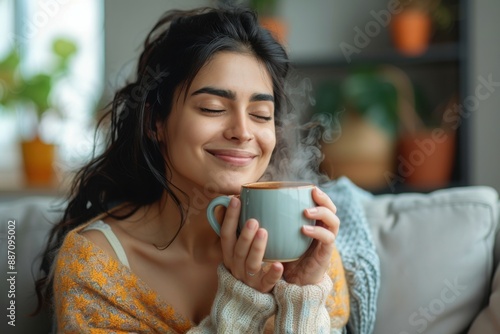 Peaceful young indian lady sitting on couch with closed eyes, enjoy drinking coffee, enjoying morning with warm drink in living room, copy space
