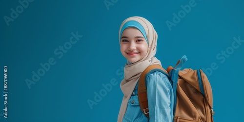 Smiling muslim girl with a school backpack on her back, isolated on a blue background, space for text. Concept of education and back to school.