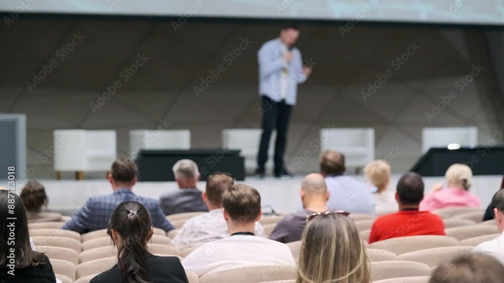 Speaker presents at a business conference in a modern venue with an attentive audience listening. Focus is on the audience. Speaker presents at a business conference in a modern venue with an attentive audience listening. Focus is on the audience.