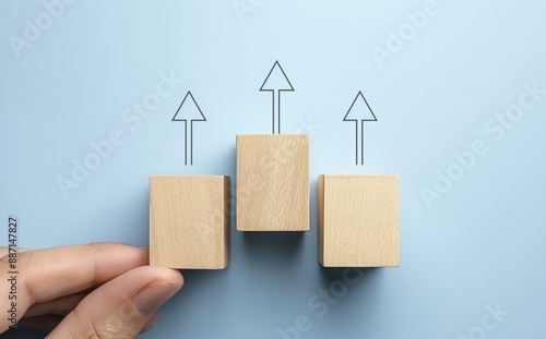 A hand is adjusting one of three wooden blocks, each with an upward-pointing arrow above them, on a light blue background. photo