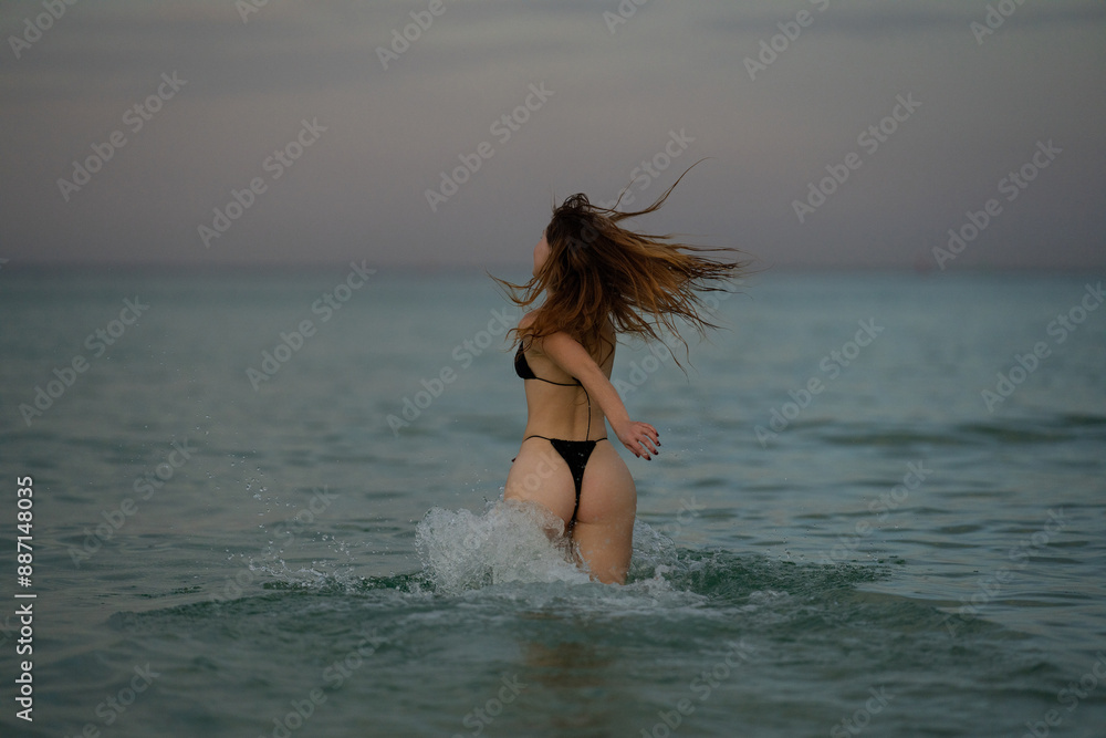 Fototapeta premium Sexy woman enjoying summer at sea. Beautiful girl in a sexy bikini on the beach. Sexy booty woman playful on paradise tropical beach. Summer girl running and splashing in sea water.