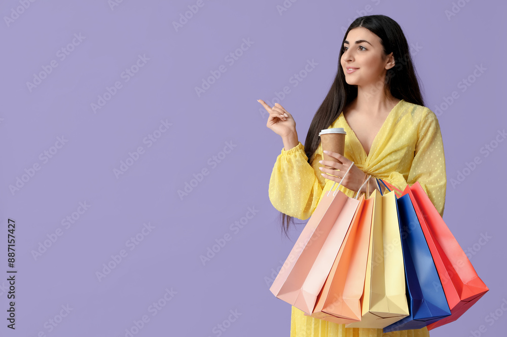 Beautiful young woman with shopping bags and cup of coffee pointing at something on lilac background Beautiful young woman with shopping bags and cup of coffee pointing at something on lilac background