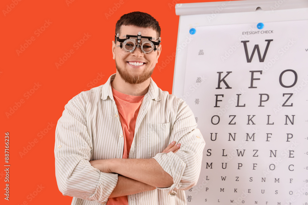 Young man in trial frame with eye test chart on red background Young man in trial frame with eye test chart on red background